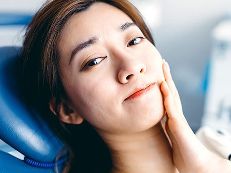 A young woman holding her jaw in pain from a retainer causing her problems.